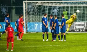 Bramkarz w żółtym stroju broni strzał. Piłkarze w niebieskich i czerwonych strojach czekają na rozwój akcji. Zastanawiasz się, ile trwa mecz piłki nożnej?